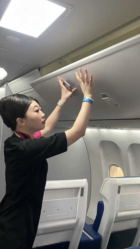 A student reaching up to the overhead compartments inside an aircraft cabin during a training visit