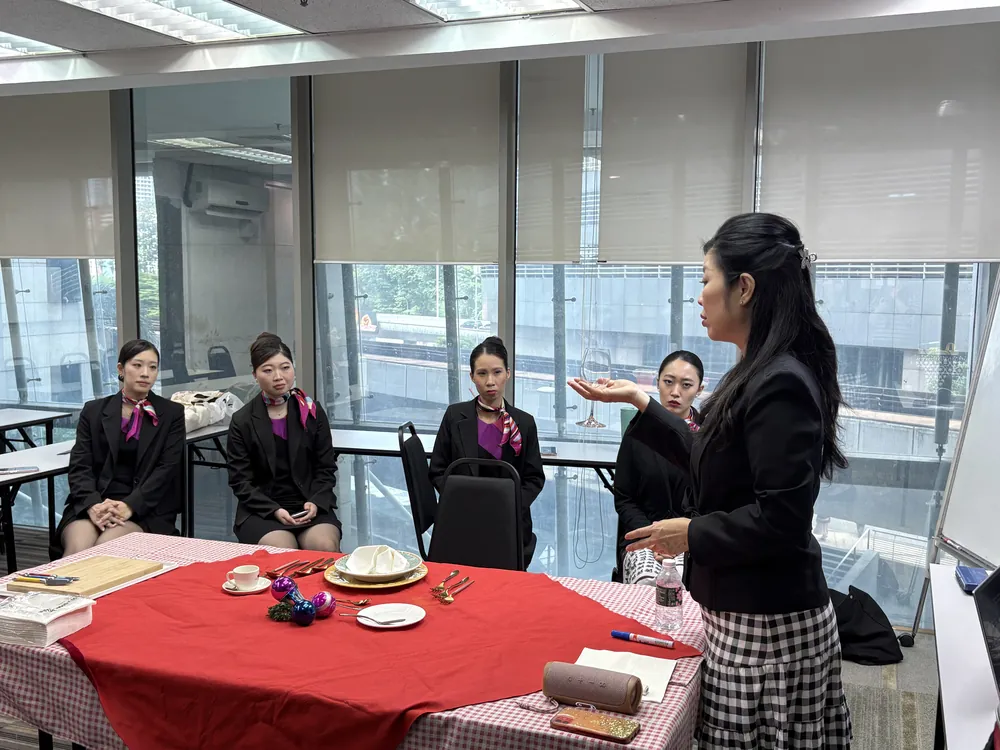 A trainer explaining table service to students seated at a covered training table