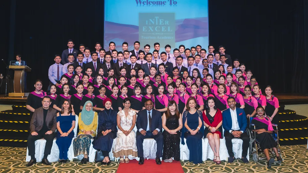 Graduates and staff on stage in front of the Inter Excel backdrop at a graduation ceremony