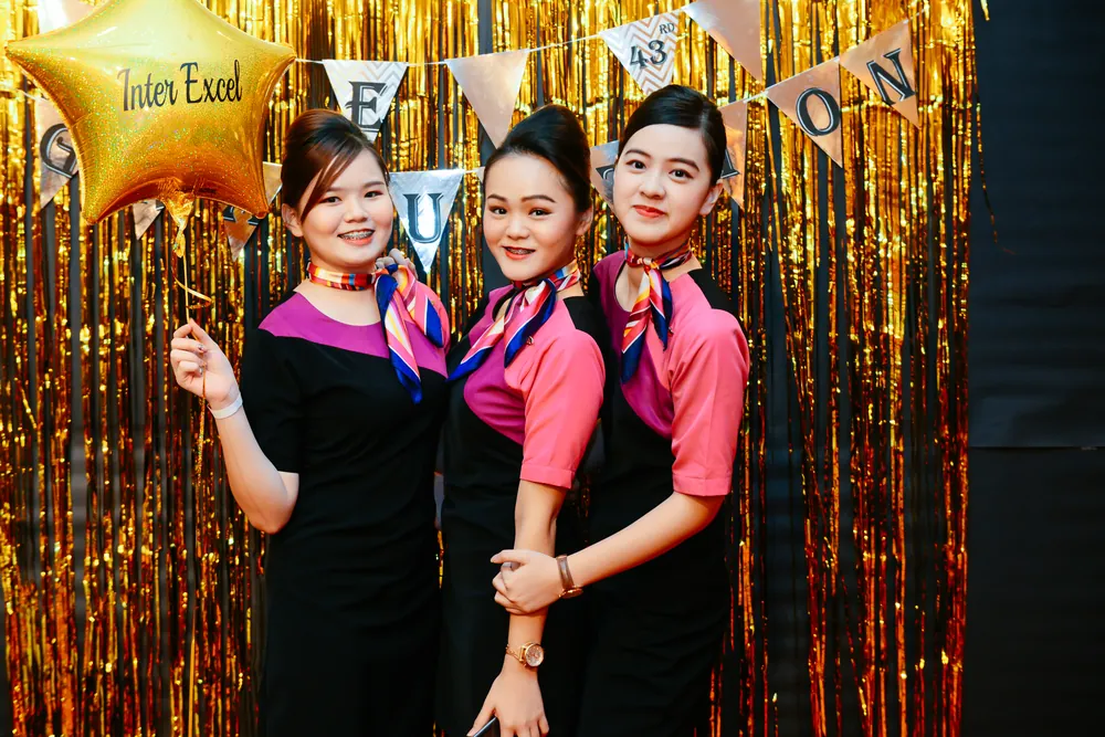 Three graduates in uniform in front of a gold backdrop holding an Inter Excel star balloon
